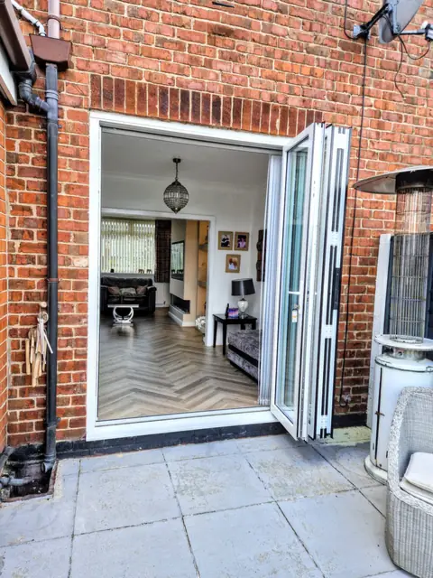 White aluminium bifold doors folded and stacked to one side of a brick opening, herringbone floor beyond