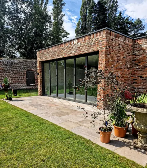 Anthracite bifold run across a brick garden room, onto a sandstone patio