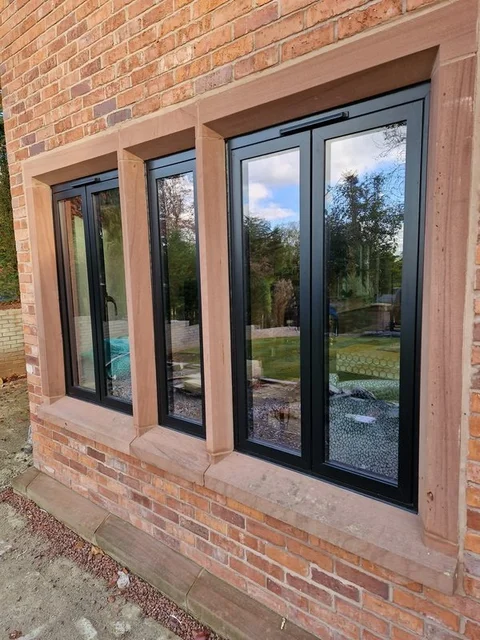 Anthracite aluminium casement windows in a brick opening with sandstone mullions and cills