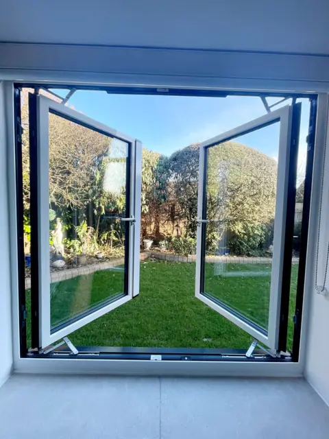 White aluminium casement pair opened outward from inside, garden beyond