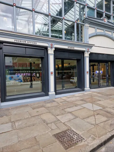 Dark aluminium shopfront screens to offices and studios under a glazed arcade