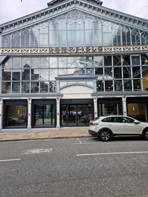 Dark aluminium shopfronts and entrance screens at street level in a historic glazed-roof building