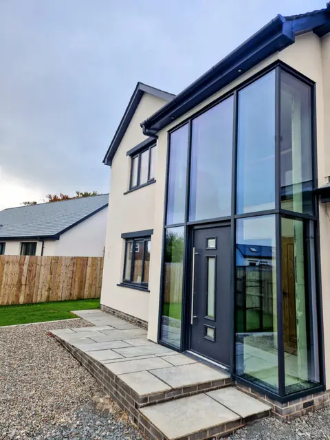 Double-height aluminium glazed entrance screen with the entrance door set into it, on a rendered house