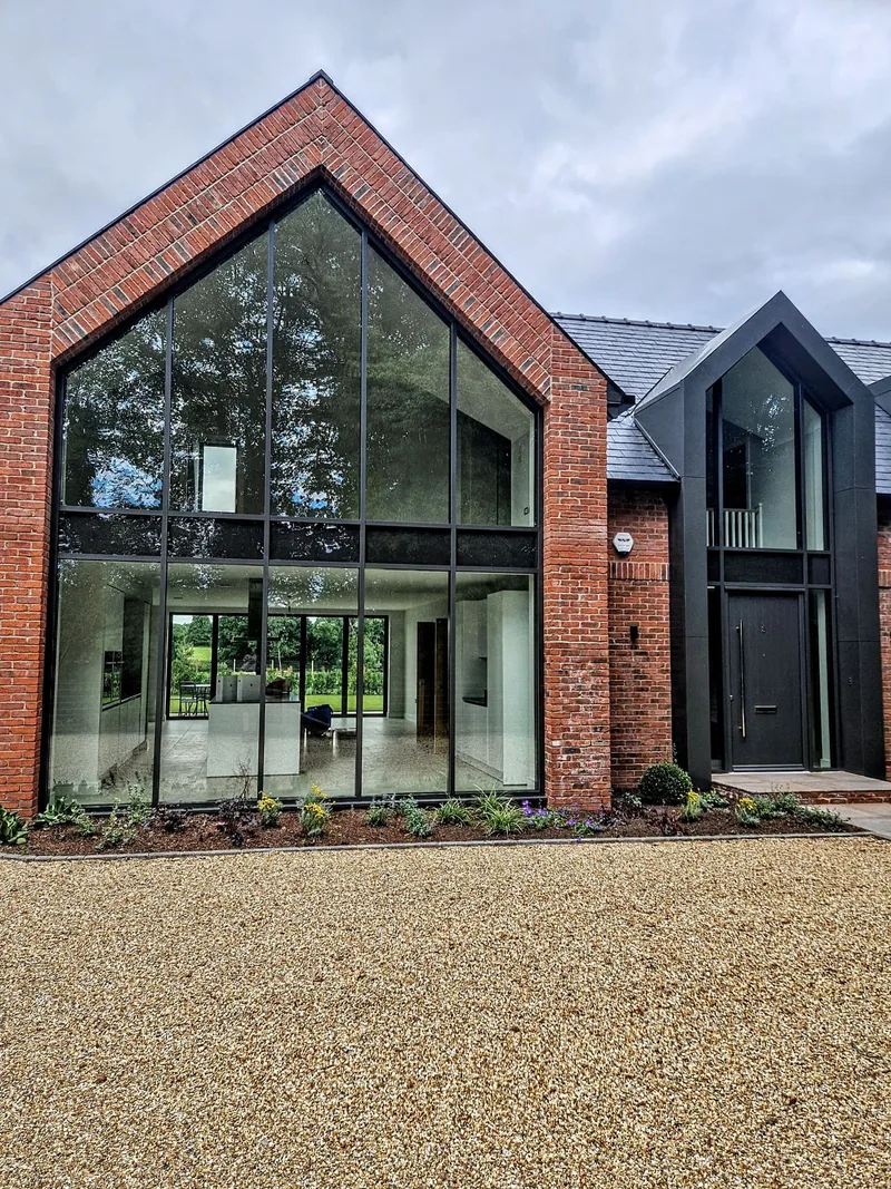 Double-height aluminium curtain walling in a brick gable, with a second glazed gable and entrance alongside