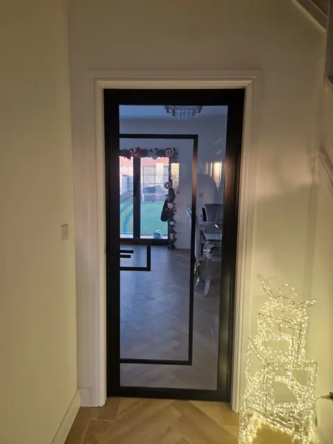 Steel-look internal door off a hallway, looking through to a herringbone floor beyond