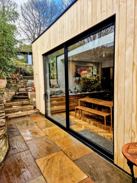 Black aluminium slider into a timber-clad garden room, sandstone patio and steps