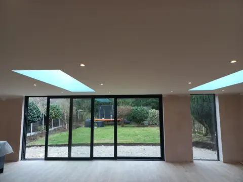 Wide black aluminium slider run seen from inside an open-plan room with rooflights